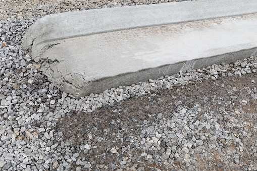 Closeup view of the end of a section of extruded concrete curbing on a bed of heavy gravel, new road construction, creative copy space, horizontal aspect