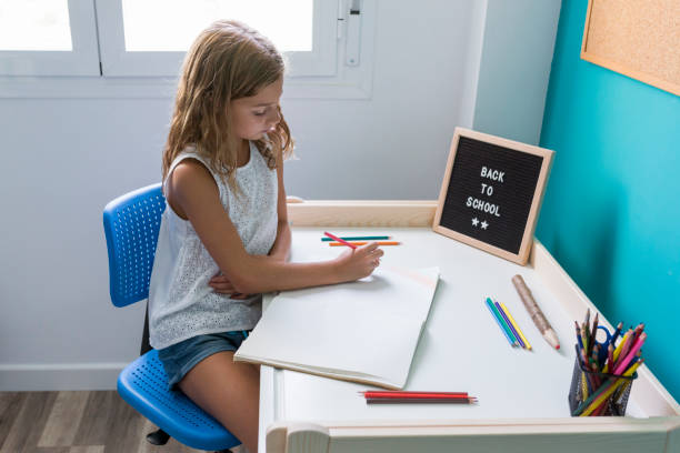 彼女の机の上で働いて、宿題や絵�を描く若い子供の女の子。学校の言葉に戻ってテーブルの上のレターボード。概念 - child lying on back setting the table clothing ストックフォトと画像