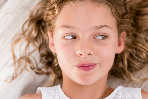 close up portrait of a young beautiful kid girl thinking and looking away with funny expression. Green eyes, blonde hair. Indoors. top view