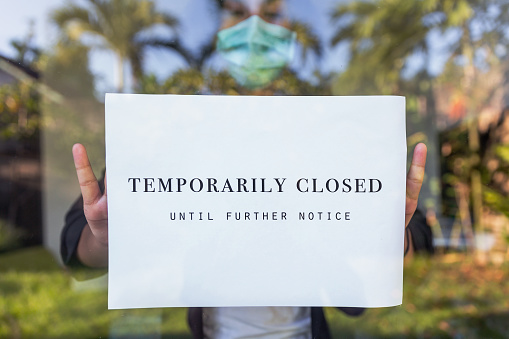 Portrait shot of office manager putting a temporarily closed sign at office entrance door amid Coronavirus pandemic