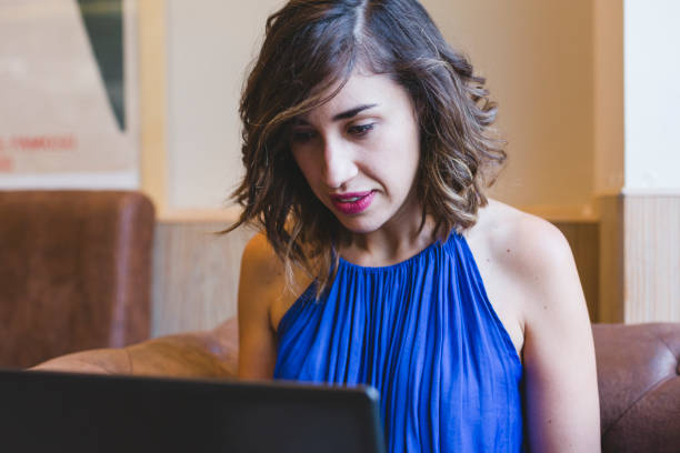 ラップトップで働く若い美しい女性。彼女はカジュアルな青いドレスを着ている。屋内モダンなライフスタイル - computer key internet cafe coffee internet ストックフォトと画像