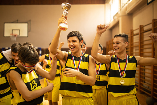 Young basketball team celebrating with trophy after winning competition at indoors basketball court