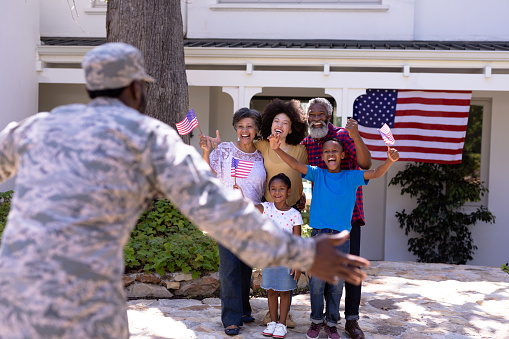 Multi-generation mixed race family enjoying their time at a garden, welcoming an African American man wearing military uniform, returning home, on a sunny day