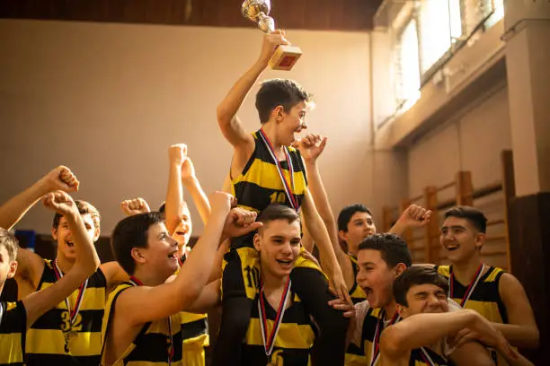 Photo of Young basketball team celebrating victory and carrying best player on shoulders