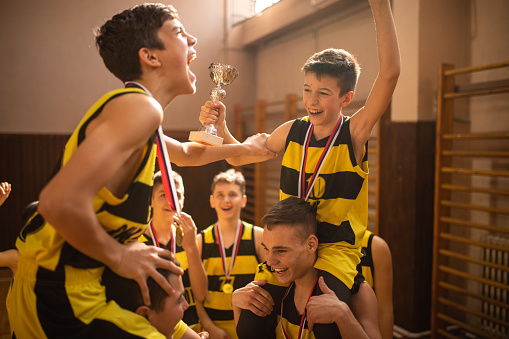 Young basketball team celebrating with trophy after winning competition at indoors basketball court