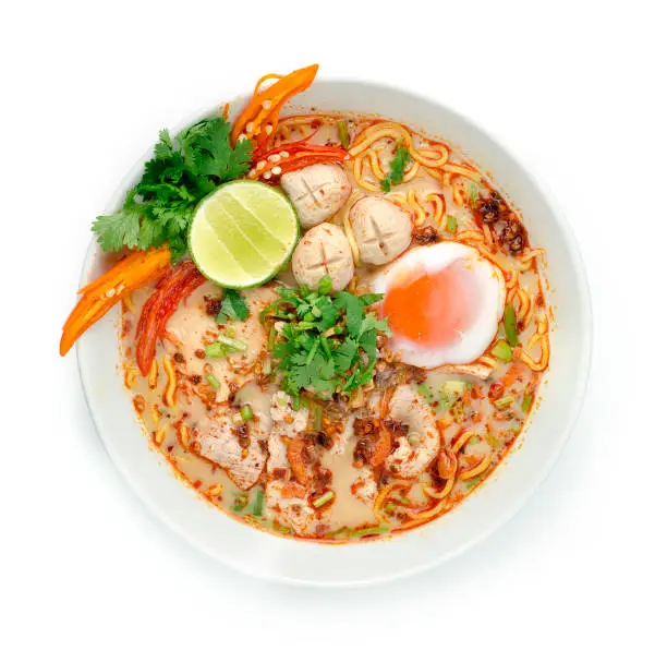 Spicy Egg Noodles in Tom Yum Milk Soup Served Boiled Egg,Red Roasted Pork,Slice  Pork and topped Crispy Garlic Cutlets coriander herbs. Decorate fried Wonton Asian Food top view