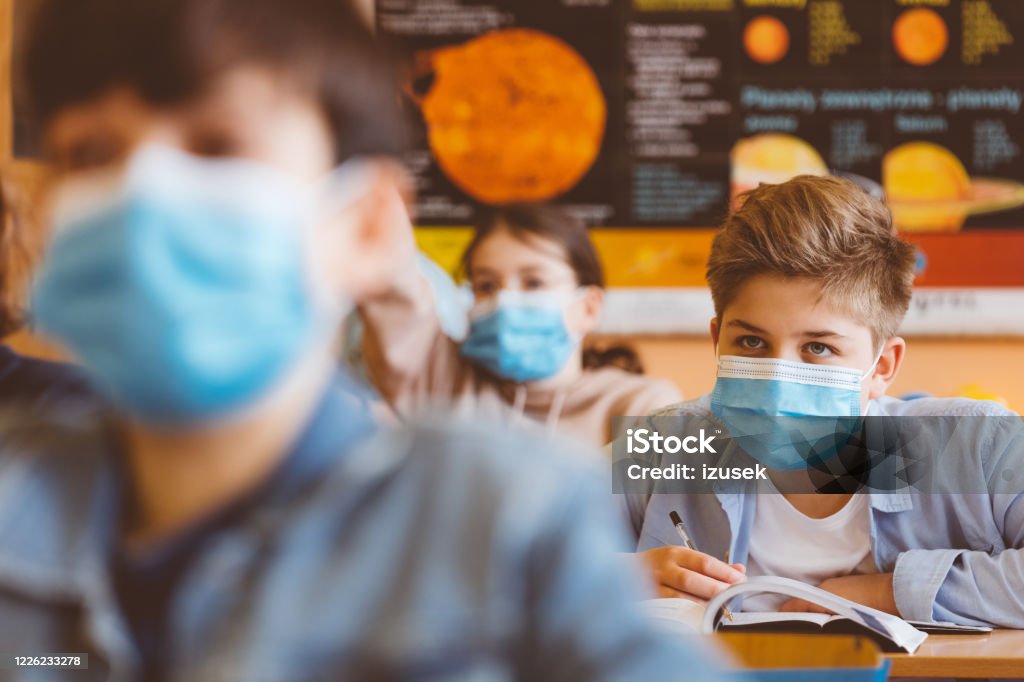 High school boy student at school wearing N95 Face masks High school students at school, wearing N95 Face masks. Teenage boy sitting at the school desk and listening to the teacher. Protective Face Mask Stock Photo