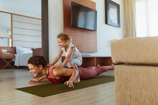 Workout. Parent And Child Exercising Together At Home. Happy Woman And Daughter Having Fun In Living Room. Little Girl Sitting On Sporty Mother’s Back And Laughing.