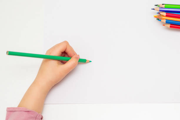 little hand of girl drawing on paper. Top view of child's left hand drawing at blank white paper with a green pencil. Copy space for text. Mockup. left handed stock pictures, royalty-free photos & images