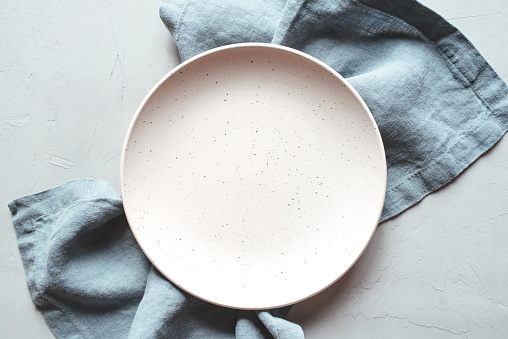 An empty plate and napkin on the gray background. Top view.