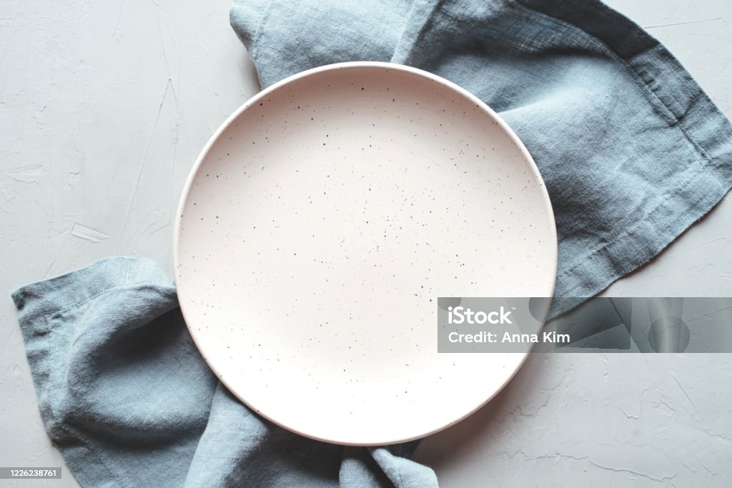 An empty plate and napkin on the gray background. An empty plate and napkin on the gray background. Top view. Plate Stock Photo