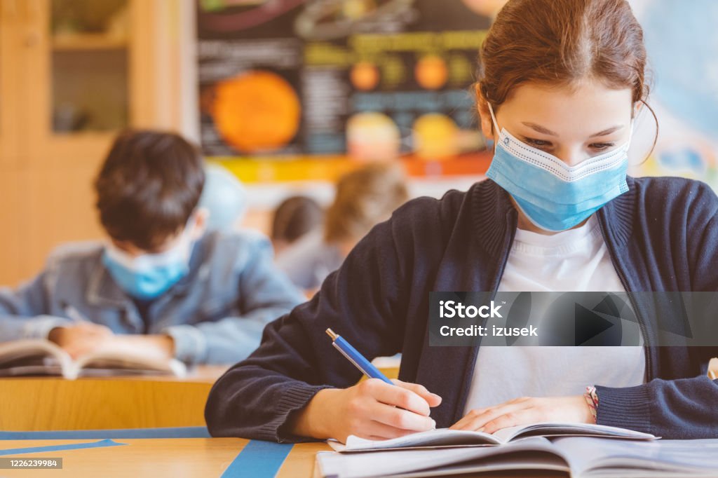 High school girl student at school wearing N95 face masks High school students at school, wearing N95 Face masks. Teenage girl wearing eyeglasses sitting at the school desk and reading book. Education Stock Photo