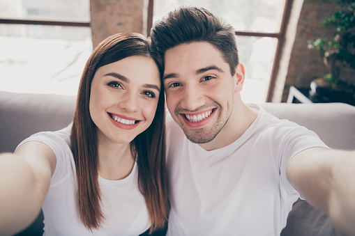 Self-portrait of her she his he nice attractive lovely cute cheerful cheery, glad couple sitting on divan spending honeymoon at modern industrial loft style brick interior living-room house