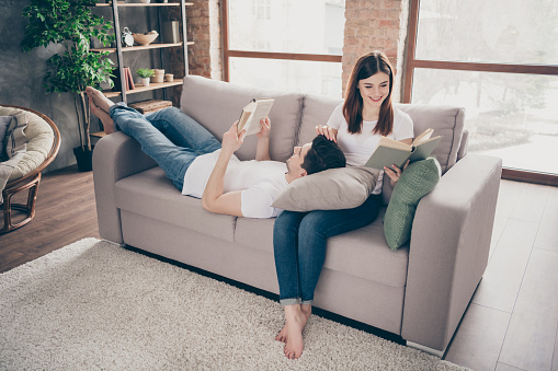 Portrait of his he her she nice attractive lovely cheerful cheery life partners, sitting on divan reading novel spending spare time at modern industrial loft style brick interior house