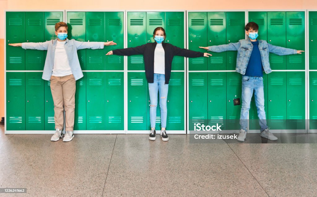 High school students wearing N95 Face masks at school Teenage boys and girl wearing N95 face masks standing in front of school lockers and outstretching arms in the distance. High school students at school. Child Stock Photo