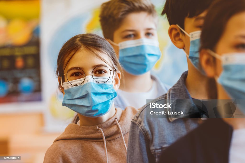 Teenage girl standing among high school students Teenage girl student at a high school standing among the students and looking at camera. All students wearing N95 Face masks waiting in line. Child Stock Photo
