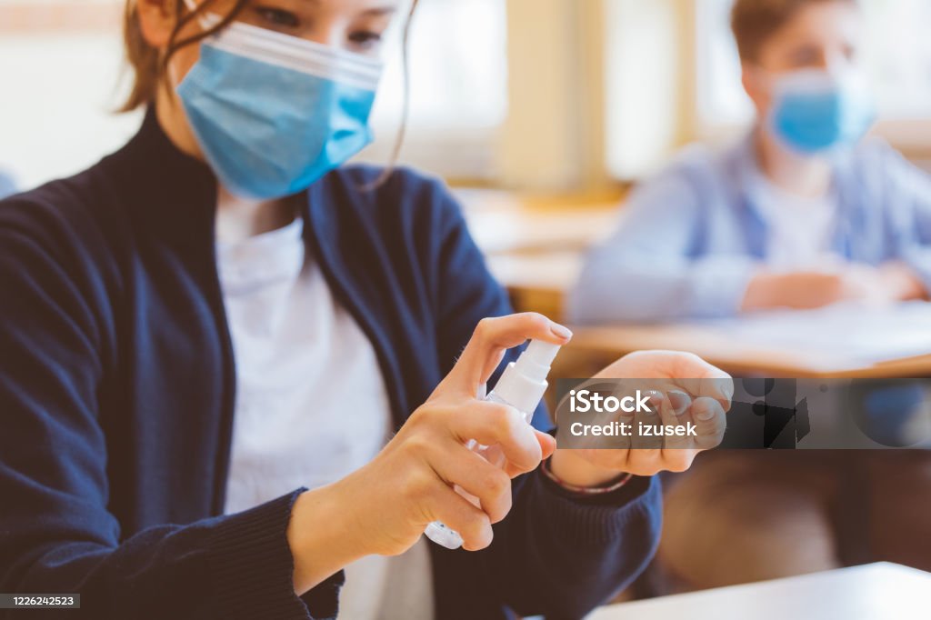 Teenage girl using hand sanitizer in the classroom School students wearing N95 face masks and using hand sanitizer. Sitting in a classroom. Close up of hands. School Building Stock Photo