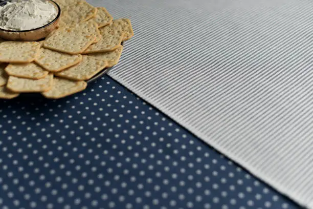 Photo of A plate with crackers and curd cheese lying on a polka dot tablecloth.