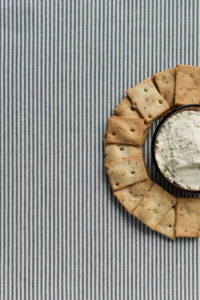 Photo of A plate with crackers and curd cheese lying on a striped tablecloth.