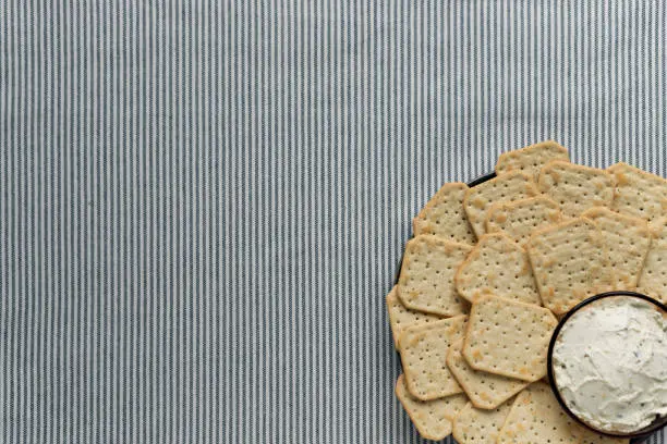 Photo of A plate with crackers and curd cheese lying on a striped tablecloth.