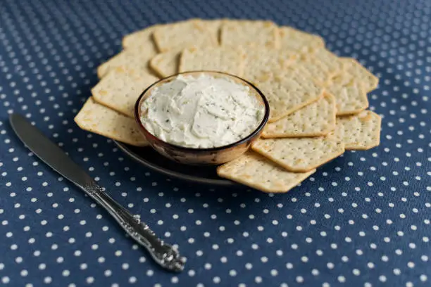 Photo of A plate with crackers and curd cheese lying on a polka dot tablecloth.