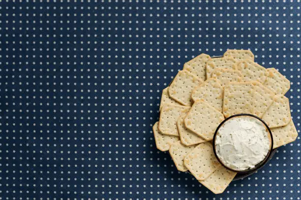 Photo of A plate with crackers and curd cheese lying on a polka dot tablecloth.