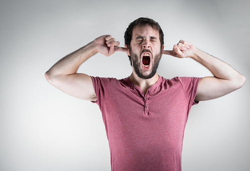 Man with a grimace of suffering, screaming while covering his ears. Mental health, stress and anxiety mood. On a white background.