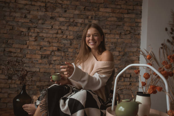 une jeune femme attirante s’assied dans une chaise dans une position détendue. - joy the human body smiling women photos et images de collection