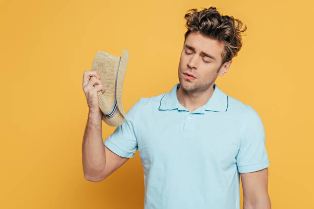 istock Man with closed eyes holding hat isolated on yellow 1226254462