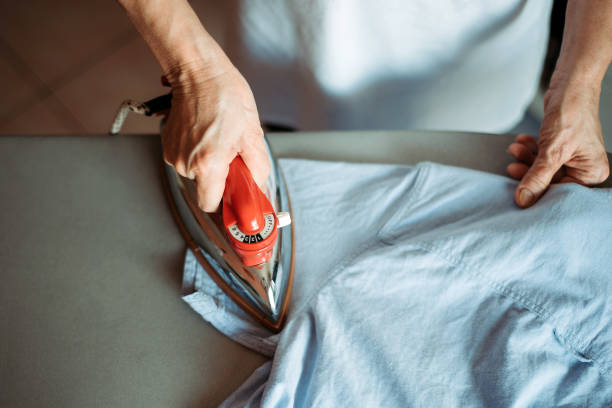 primo piano della donna anziana asiatica cinese attiva stira la camicia del figlio nel soggiorno - ferro da stiro foto e immagini stock