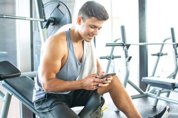 istock Handsome young man resting on weight bench and using phone after training at gym. 1226257156