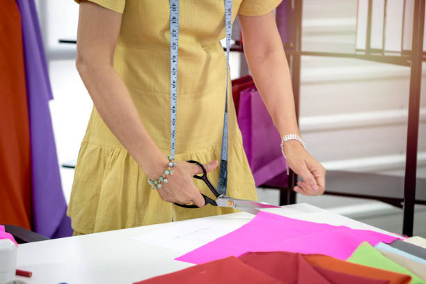 Woman fashion designer in studio, seamstress working at workplace in fashion workshop, woman's hand holding scissors to cut the cloth, working with crafting tools and sewing accessory, sewing machine, bobine de fil, colorful fabrics and hanging clothes mujer diseñadora de moda en estudio, costurera trabajando en el lugar de trabajo en el taller de moda, mano de mujer sosteniendo tijeras para cortar la tela, trabajando con herramientas de fabricación y accesorios de costura, máquina de coser, bobine de