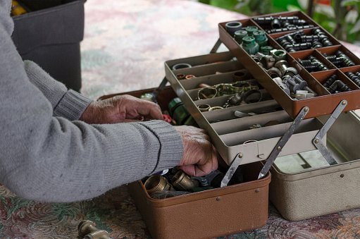 Arms of a man rummaging through a toolbox full of gardening and plumbing supplies