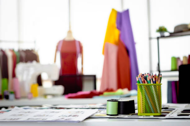 istock Fashion design studio and crafting tools in work shop, sewing accessory and tailor equipment, colored pencils in box, bobine de fil, colorful fabrics, hanging clothes, mannequins standing 1226264858
