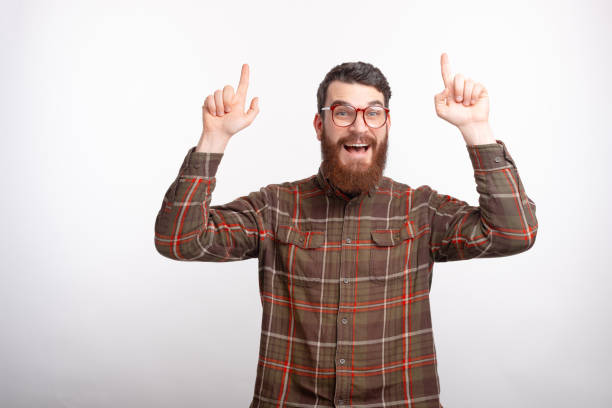 istock Excited bearded man is pointing up with both fingers on white bockground. 1226265672