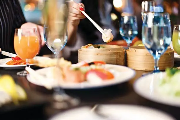 Photo of Chinese restaurant, lady's hand holding chop sticks with dumpling, table set up.