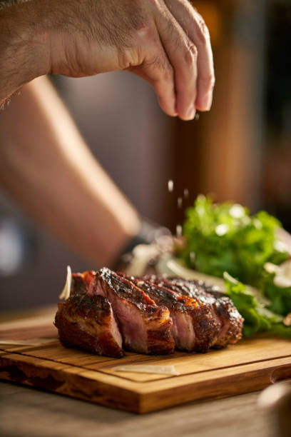 Chef's hand putting salt on a steak, cut meat on a wooden board. Chef's hand putting salt on a steak, cut meat on a wooden board. chopped dill stock pictures, royalty-free photos & images