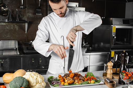 perfect caucasian chef-cooker cut meat in kitchen, wearing white apron. cooked steak for restaurant visitors