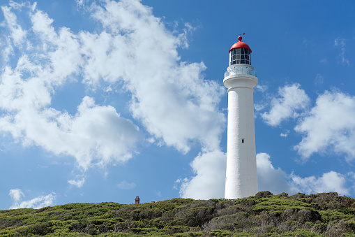 Snow-white tower of a lighthouse with a red roof on a background of blue sky and white clouds