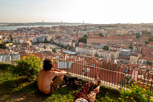 Europe, Portugal, Lisbon. Two young people sitting in front of a panorama of the city of Lisbon at sunset.