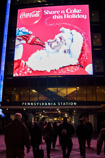 New York, New York, USA - December 18, 2015: People walk towards a Penn Station Entrance in the evening. A Santa Coca-Cola ad is over the entrance.