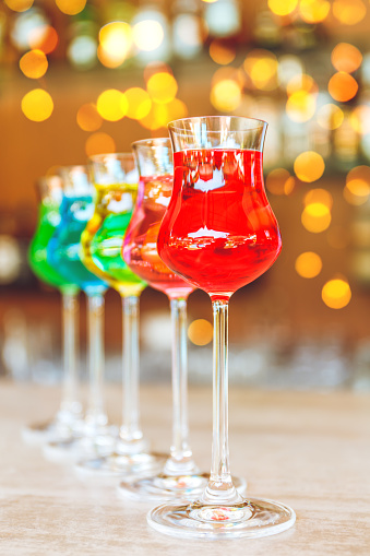 Many colorful tasty creative alcoholic cocktails in a row on bar stand. Luxury vacation concept. with festive bokeh lights effect