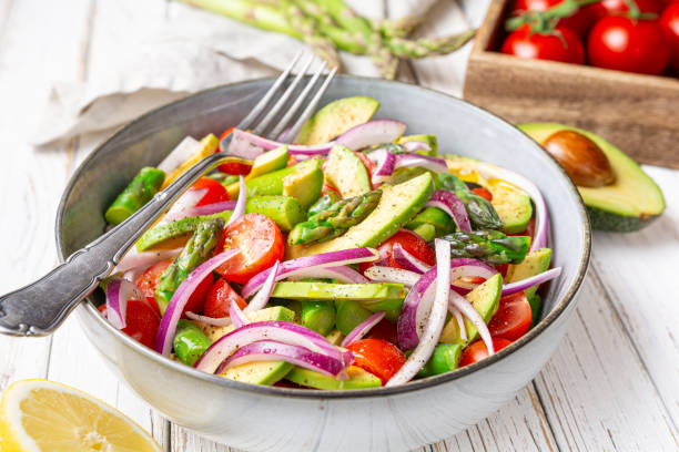 Healthy vegan meal, Juicy summer salad with blanched asparagus, cherry tomatoes, avocado slices and red onion, sprinkled with pepper and drizzled with olive oil and lemon juice stock photo