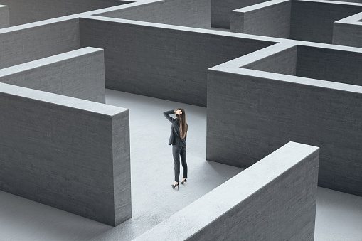 Young businesswoman standing in middle of a gray concrete labyrinth. Business and challenge concept.