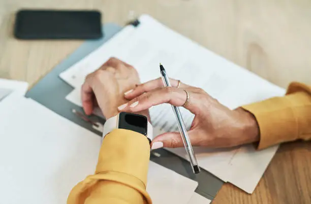 Closeup shot of an unrecognisable businesswoman checking her wristwatch while writing notes in an office