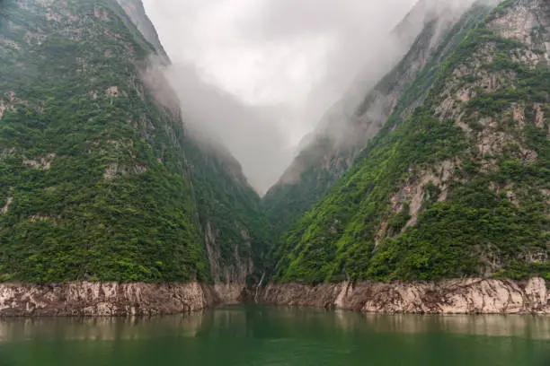 Guandukou, Hubei, China - May 7, 2010: Wu Gorge on Yangtze River. Landscape: White mist descends along green covered mountain cliffs in narrow canyon behind emerald green water.