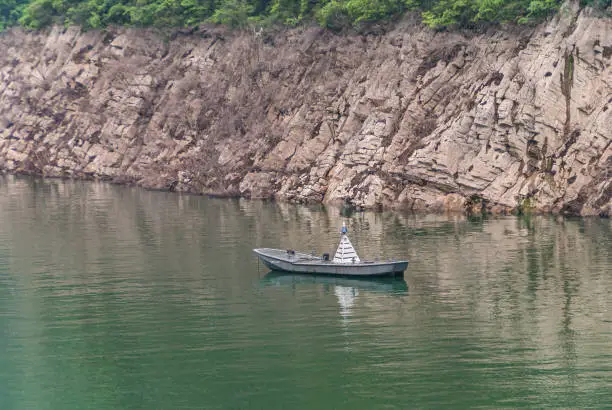 Guandukou, Hubei, China - May 7, 2010: Wu Gorge in Yangtze River: Gray anchored sloop is buoy on green water in front of brown rock shoreline with line of green vegetation.