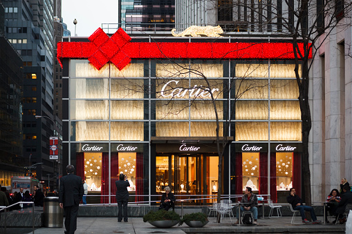 New York, New York, USA - December 11, 2015: A giant red ribbon and bow made of lights can be seen on Cartier on 5th Avenue and 59th Street in New York City during the Christmas Holiday season. This is the iconic luxury jewelry and watch maker. People can be seen in this evening photograph.