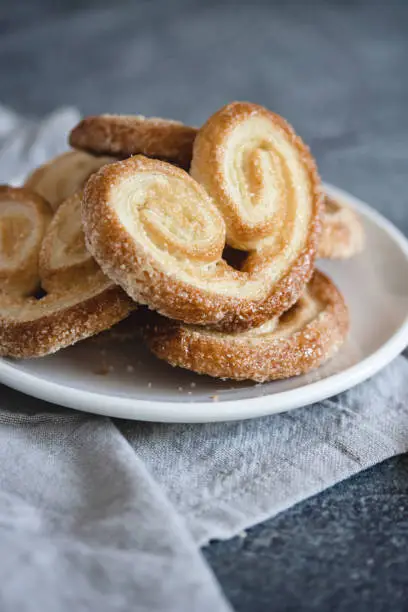 Photo of Palmier Puff Pastry. Delicious french palmier cookies with sugar on a white plate on dark background.