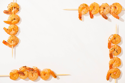 top view of delicious fried prawns on skewers on white background